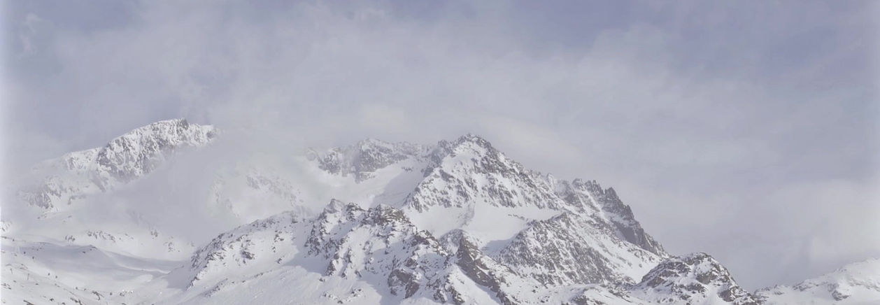A snow-covered mountain range under drifting cloud, its ridgeline pale against the sky.